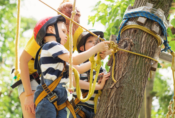 Two boys at an adventure park inspecting a rope with an instructor