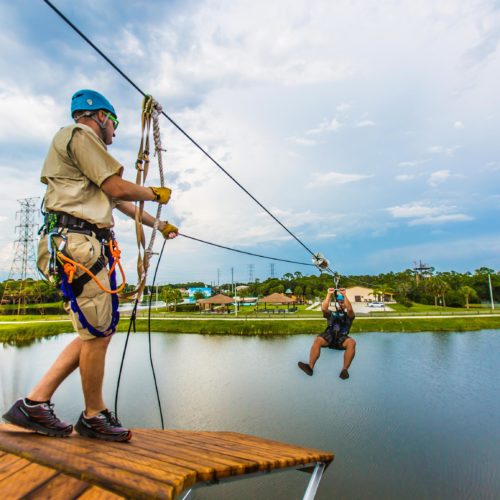 Zip line course instructor guides a man across a lake